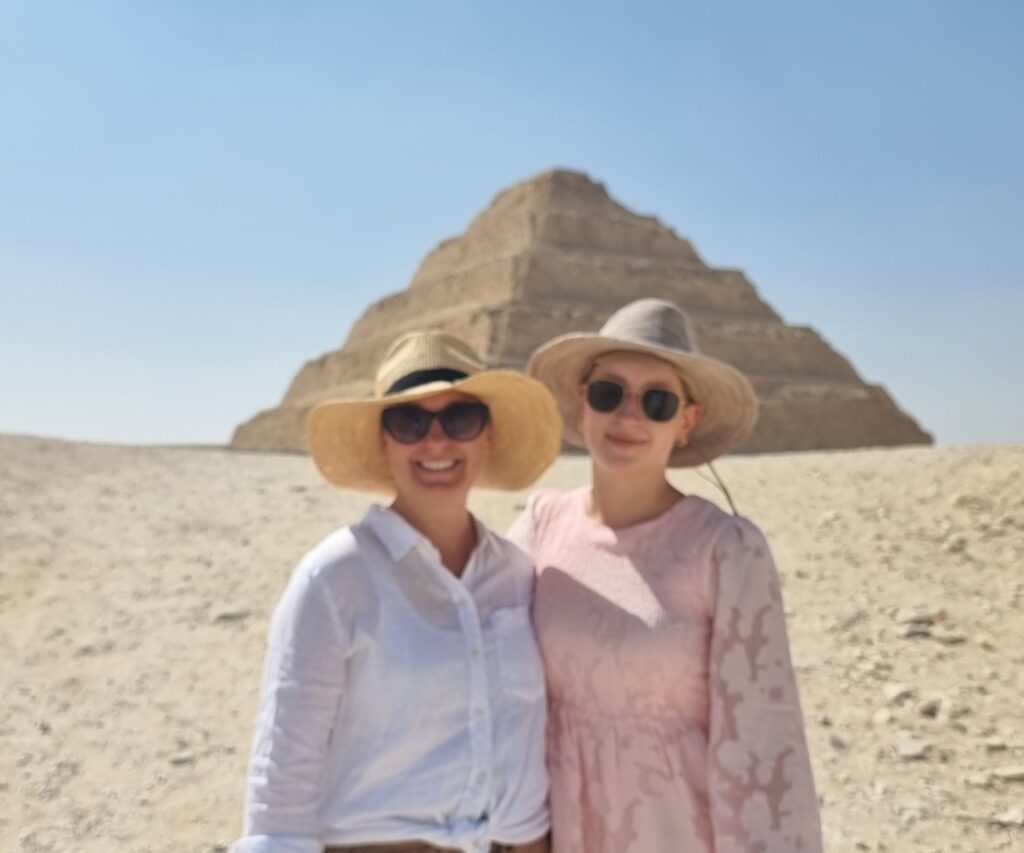 a photo showing 2 tourists taking a photo with the step Pyramid in Egypt